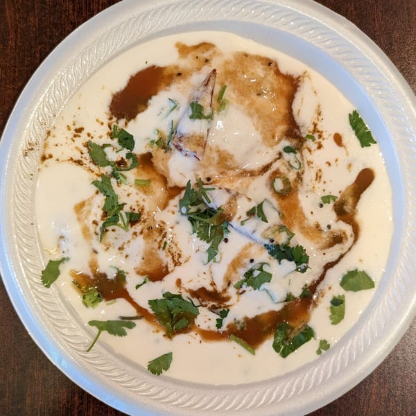 Dahi Bhalla, a popular Indian snack, with yogurt, tamarind chutney, and cilantro on a white plate.