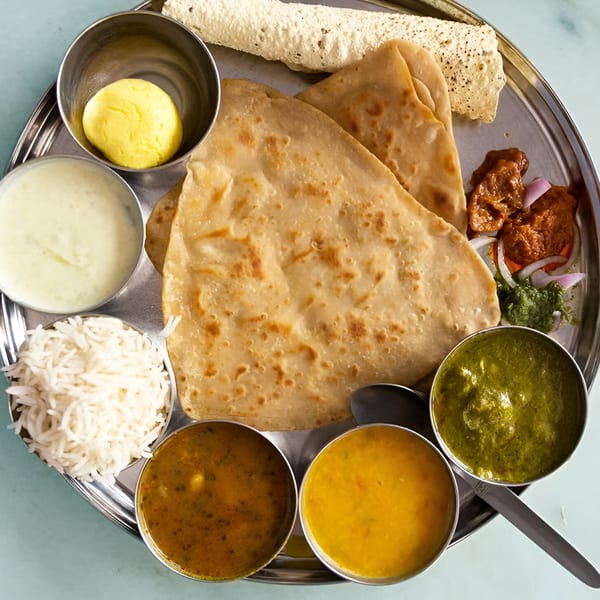 Overhead view of an Indian thali with paratha, rice, papadum, curries, and a yellow dessert.