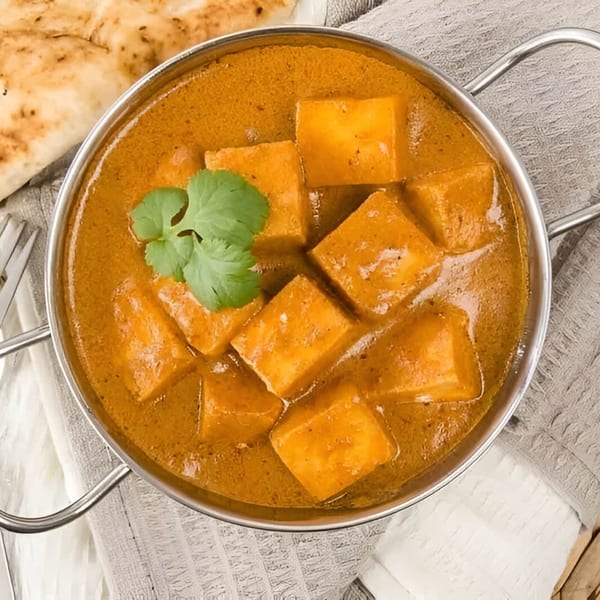 Overhead view of paneer butter masala in a metal bowl, garnished with cilantro, with naan bread.