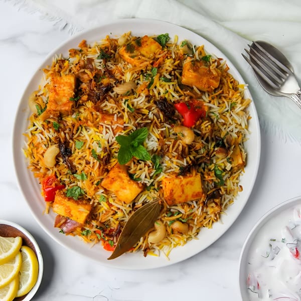 Paneer Biryani from India X, with rice, paneer, cashews, and mint, served with raita and lemon.