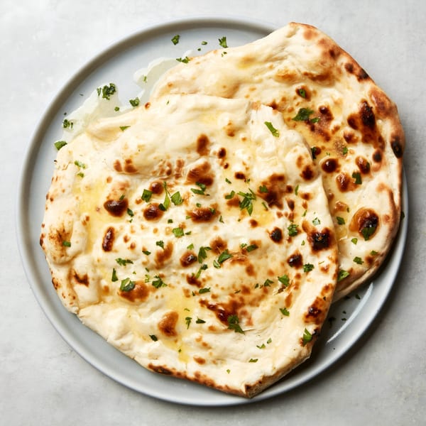 Two pieces of golden-brown Indian naan bread, drizzled with butter and sprinkled with fresh parsley.