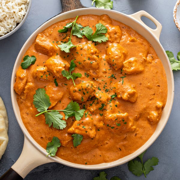 Overhead view of a pan of Indian butter chicken, garnished with fresh cilantro, with rice and naan.